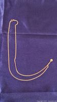 Full-length view of chain and pendant on blue fabric background