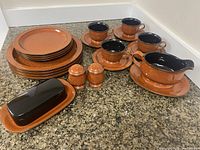 Full set of the Mikasa Chromatic Terracotta dinnerware including plates, cups, saucers, gravy boat, butter dish, and salt and pepper shakers arranged on countertop.