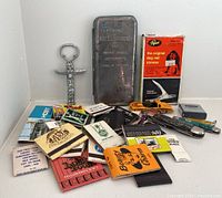 Photo, overview of all items: pocket knives, matchbooks, bottle opener, pet nail trimmer, Hot Wheels, tape measure.