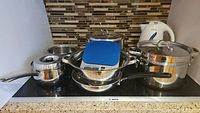 Overview of pots, skillet, steamer, colander, food scale, kettle arranged on stove top