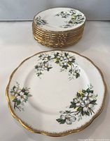 Stack of 10 Royal Albert White Dogwood bone china side plates with floral design and gold rim, and 1 luncheon plate in front showing detailed floral pattern and scalloped gold edge.
