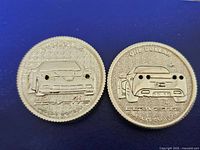 Two sterling silver coins with embossed Corvette car designs, one showing front and the other showing rear. Red light holes are visible on headlights and taillights.