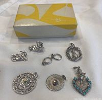 Top-down view showing all seven vintage sterling silver charms with box in background