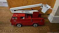 Side angled view of red Tonka fire truck with extended white snorkel arm and bucket, showing the overall size and condition.