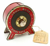 Front view of 1920s-30s red and black tin coin bank with 'Vault Bank 3 Dial Safe Lock' text and combination dial lock attached with original paper tag showing combination instructions.