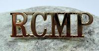 Close-up front view of RCMP metal shoulder title showing polished silver-tone letters on stone background.