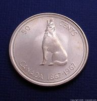 Front side of 1967 Canadian 50 cents coin showing a sitting howling wolf and inscriptions.
