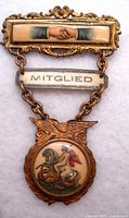 Full detailed front view of the entire medal pin showing all three components connected by chains: handshake bar, 'MITGLIED' bar, and Saint George slaying dragon medallion with eagle frame.