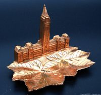 Copper-tone figural pin tray shaped like maple leaf with Parliament Buildings model on top