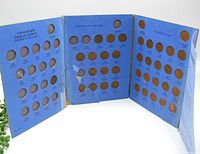 Blue cardboard coin folder opened wide showing dated holes for Canadian small cents pennies from George V to Elizabeth II eras, filled with coins.