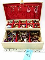 Open vanity box filled with assorted jewelry pieces showing top and bottom compartments with multiple rings, earrings, and bracelets.