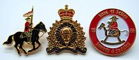 Front view showing three enamel pins related to the RCMP Musical Ride. Pins depict a mounted officer, RCMP emblem, and a circular Sons et Sellés pin.