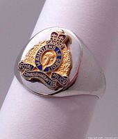 Close-up image showing the front angle of a sterling silver pinkie ring with a gold plated and blue enamel Royal Canadian Mounted Police badge crest mounted on top.