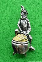 Front view of a silver-toned leprechaun pin sitting on a pot of gold against green felt background.