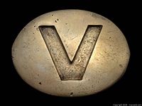 Front view of vintage brass belt buckle showing large raised 'V' symbol and signs of age wear.