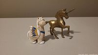 Photo showing two small figurines: a pottery horse with colored wing detail and a bronze unicorn.