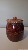 Front view of brown pottery cookie jar with embossed 'Cookies' lettering showing chip on the letter 'k'.