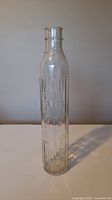 Full view of tall clear glass bottle showing embossed Shell Oil logo and text along its length on a neutral background.