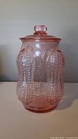 Front view showing three-dimensional peanut embossing and 'PLANTERS' lettering on pink glass jar with lid