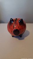 Front view of the Blue Mountain Pottery piggy bank showing the rounded orange body, black snout, ears, and feet, with coin slot on top.