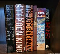 Photo of six books by Stephen King and Richard Bachman aligned vertically on a shelf showing the spines.