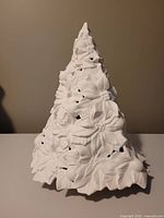 Full side view of white ceramic poinsettia tree sculpture showing detailed raised poinsettia leaves, cutouts, and pointed top.