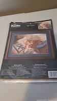 Photo of the sealed Bucilla cross stitch kit featuring the Golden Dreams design of a golden retriever dog lying down with a kite overhead on printed canvas.
