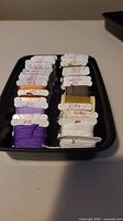 Overview of the cross stitch threads in bobbins, showing color codes and organization in a black tray.