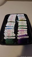 Photo shows an assortment of 22 different DMC 500 series cross stitch thread bobbins in a box. Threads colors vary from green, purple, blue, and neutrals.
