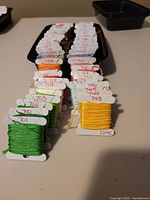 Two photos showing a collection of DMC 700 series embroidery floss skeins neatly wound on white bobbins with DMC number labels.