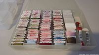 Top-down view of white plastic bobbins wound with various DMC embroidery thread colors, neatly arranged in the storage container compartments.