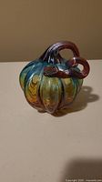 Front and side views of a small hand-blown glass pumpkin with blue, amber, and black coloring.