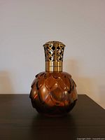 Front view of amber colored Lampe Berger artichoke style fragrance lamp showing decorative lattice gold-tone metal top and textured glass body.