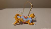 Side view of Lenox porcelain carousel cat ornament showing orange tabby color and decorative saddle with hanging string.
