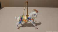 Side view of Lenox porcelain carousel goat ornament showing colorful saddle and gold hanging string.