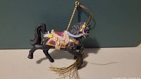 Front and side view of black porcelain carousel horse ornament showing detailed saddle and facial features, hanging loop with gold tassel