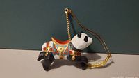 Porcelain panda carousel ornament front view showing colorful saddle and gold hanging string.