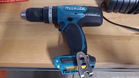 Side view of the Makita cordless drill showing blue and black body and metal belt clip.