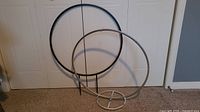 Two metal hoops on carpet; black hoop with stakes, silver hoop with circular base