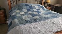 Quilt spread out on king size bed showing jean patchwork in multiple blue tones and the stitching pattern.