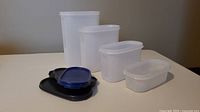 Four Tupperware containers in various sizes with respective matching lids placed in front of them, on a flat surface.