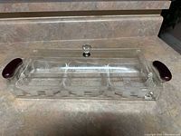 Transparent rectangular 3-section serving tray with clear lid and dark handles, displayed on countertop.