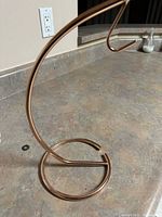 Copper banana stand with a circular base and curved hook for hanging bananas.