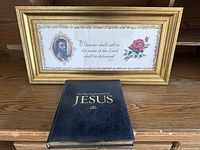 Framed religious print with portrait and rose alongside closed hardcover book titled 'In the Footsteps of Jesus'.