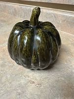 Dark green glazed ceramic pumpkin on a countertop for decorative use.