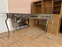 Wide angled photo showing the glass top console table with black metal frame and the rectangular mirror leaning against a wooden cabinet.