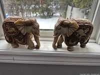 Pair of carved elephant figurines placed on a window sill, showing detailed pattern work and paint.