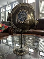 Front view of metal fish sculpture on stand showing etched details and blue enamel center.