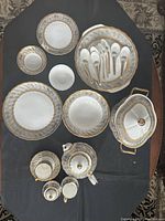 Top-down view of entire dinner and tea set arranged on black surface showing plates, bowls, cups, teapot, sugar bowl, creamer, serving spoons, and large covered serving dish