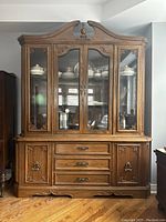Front view of a large wood and glass display cabinet with ornate carvings and three drawers in the middle.